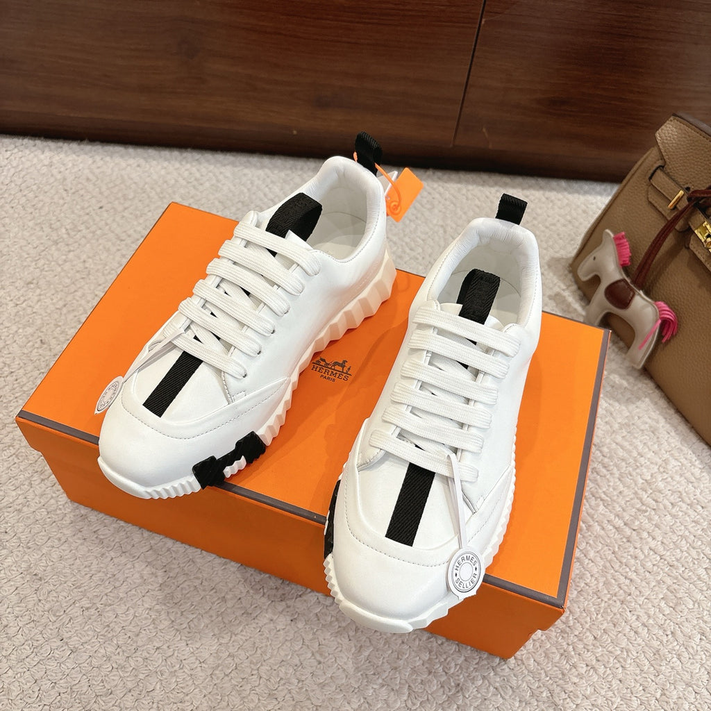 White Hermes sneakers with black stripe panels and chunky tread sole, side view on box.