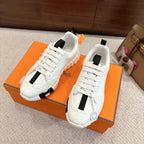 White Hermes sneakers with black stripe panels and chunky tread sole, side view on box.