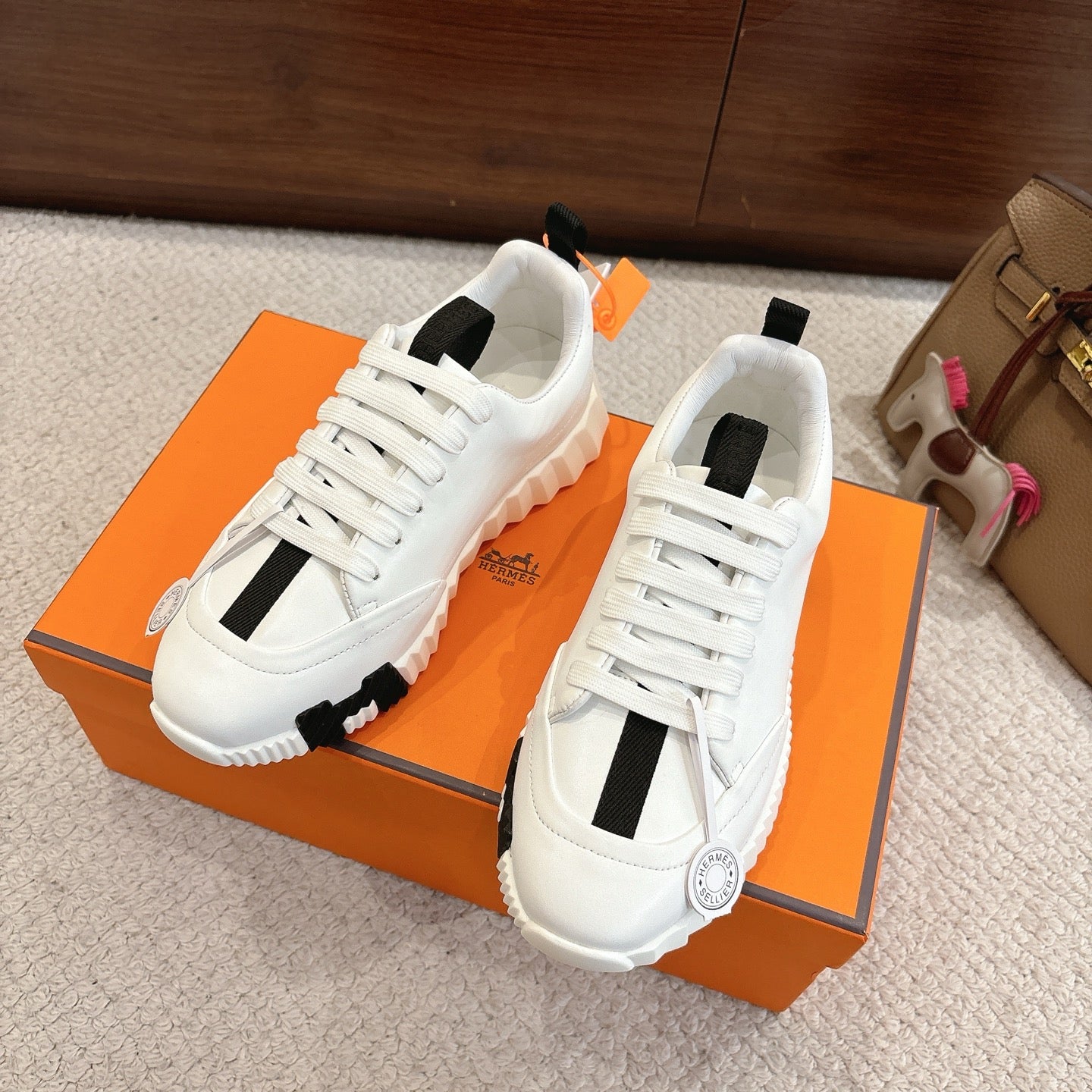 White Hermes sneakers with black stripe panels and chunky tread sole, side view on box.
