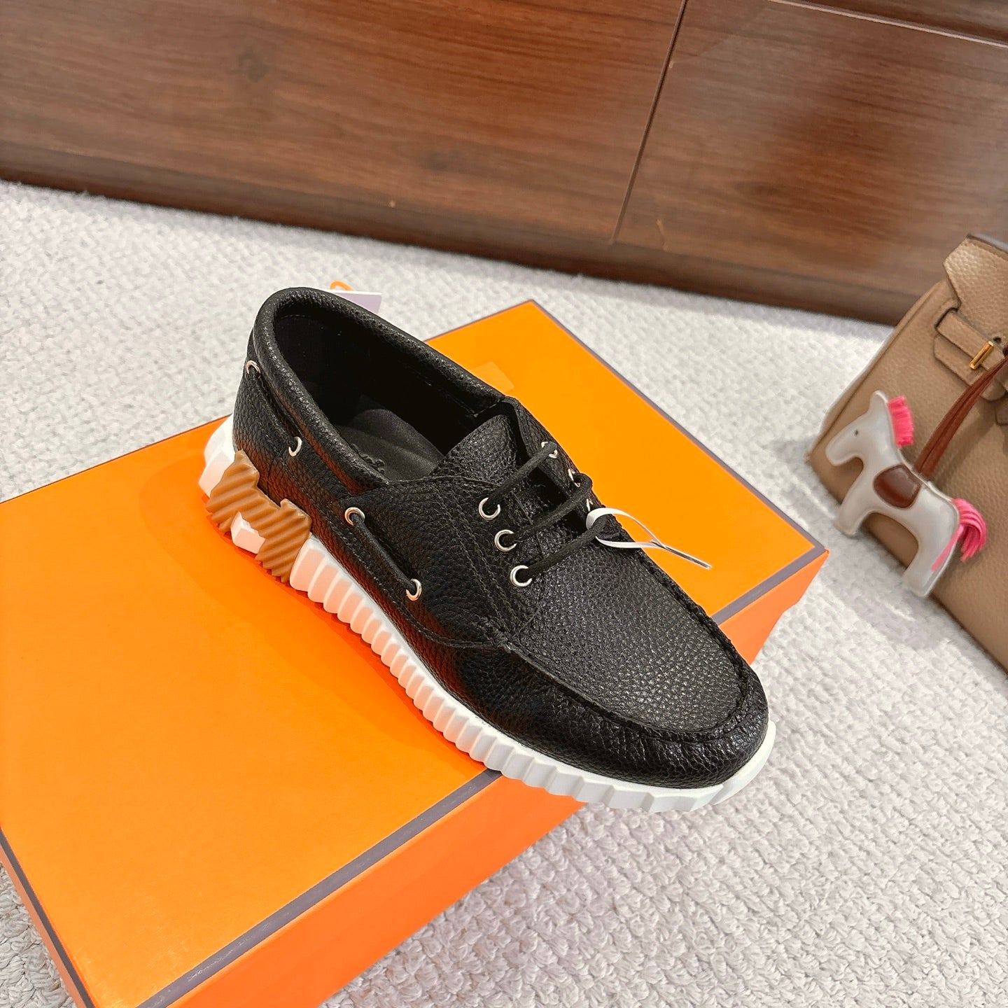 Black leather lace-up shoes with white textured sole, angled view on orange box.