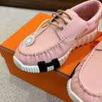 Pink leather sneaker close-up, lace-up with round logo tag and chunky white sole.