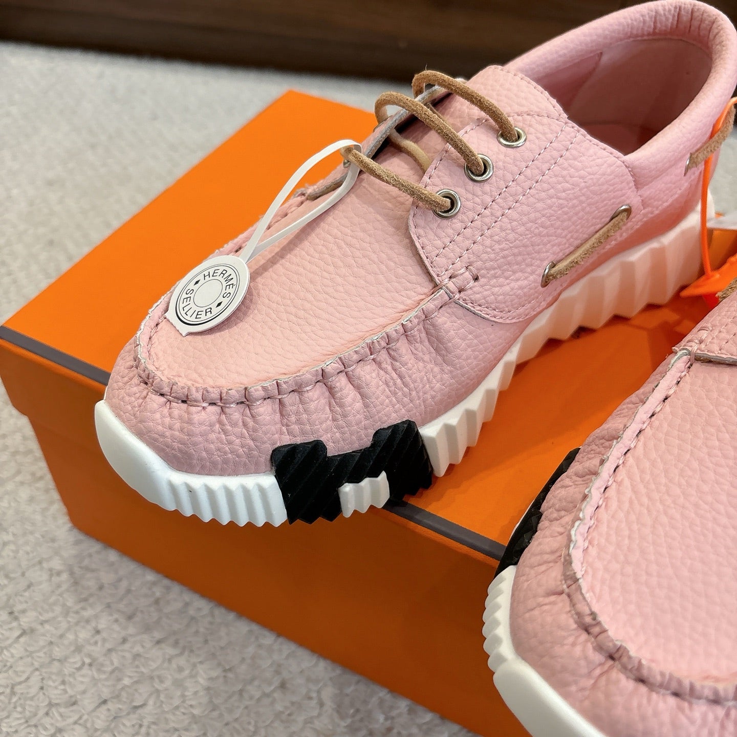 Pink leather sneaker close-up, lace-up with round logo tag and chunky white sole.