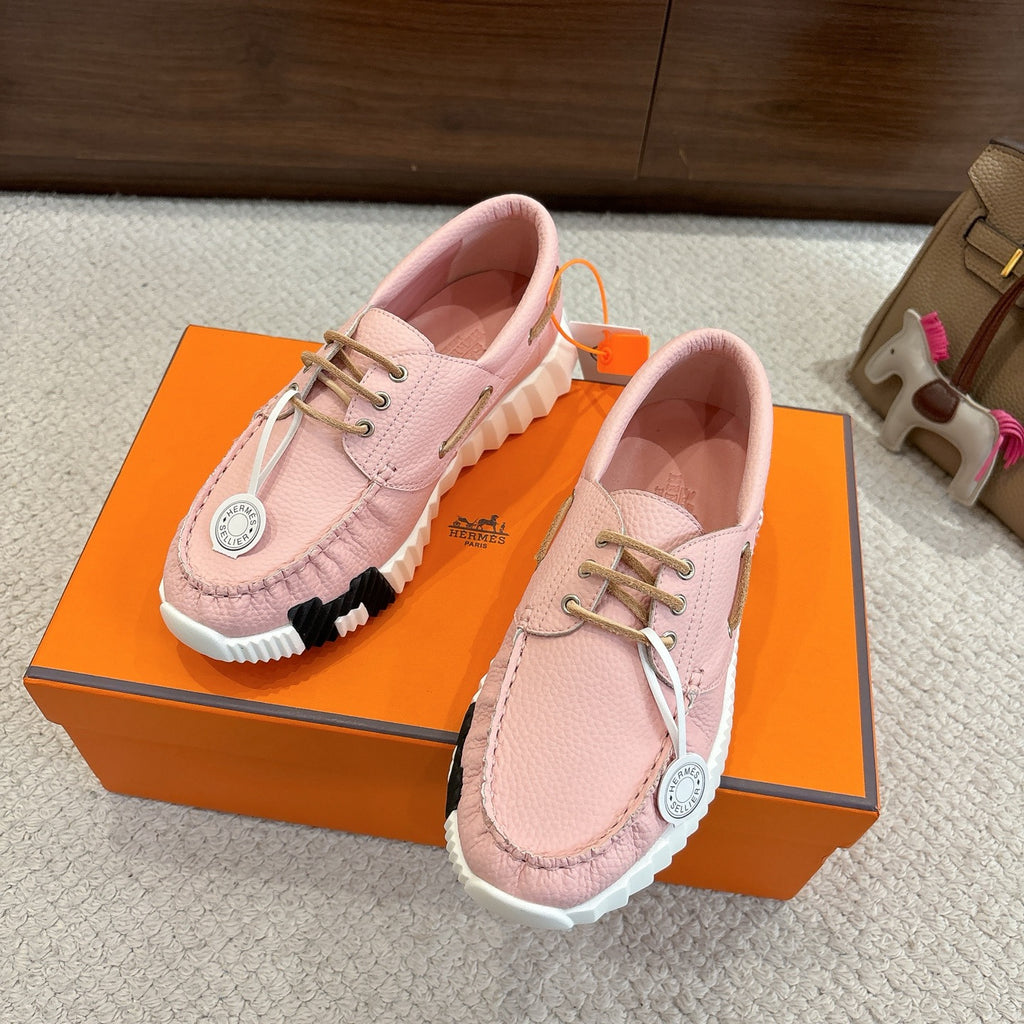 Pink leather unisex sneakers on an orange box, lace-up front with white ridged sole.