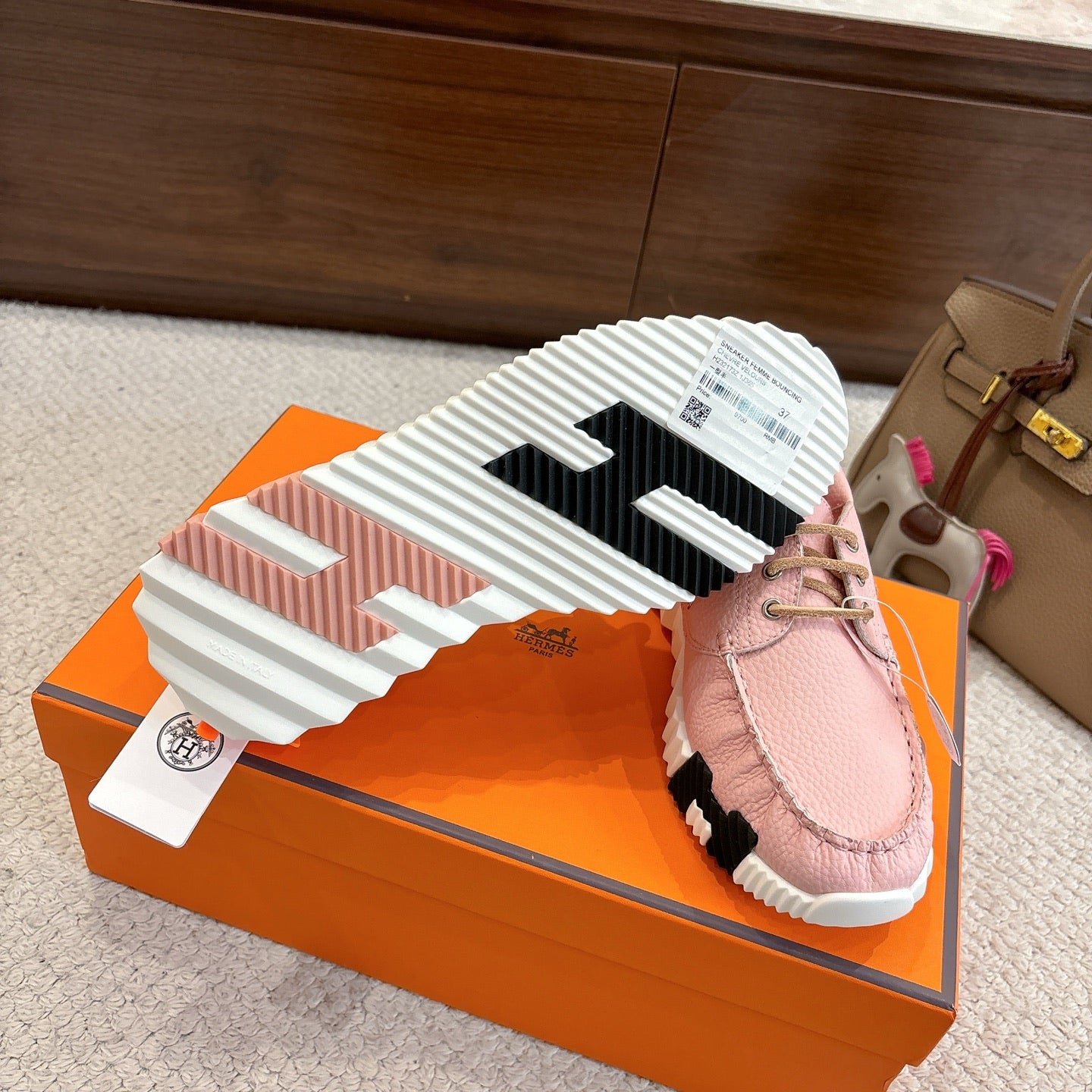 Pink leather sneaker sole view, striped rubber tread and lace-up upper.