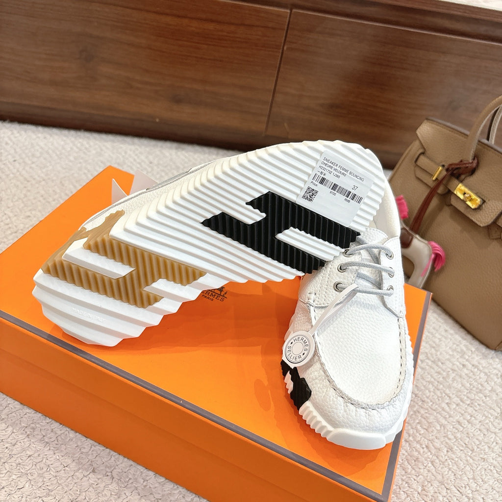 White sneaker outsole view with black tread segments and side logo patch