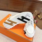 White sneaker outsole view with black tread segments and side logo patch