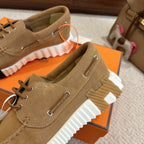 Tan suede lace-up sneakers with white ribbed sole and orange lace loop detail