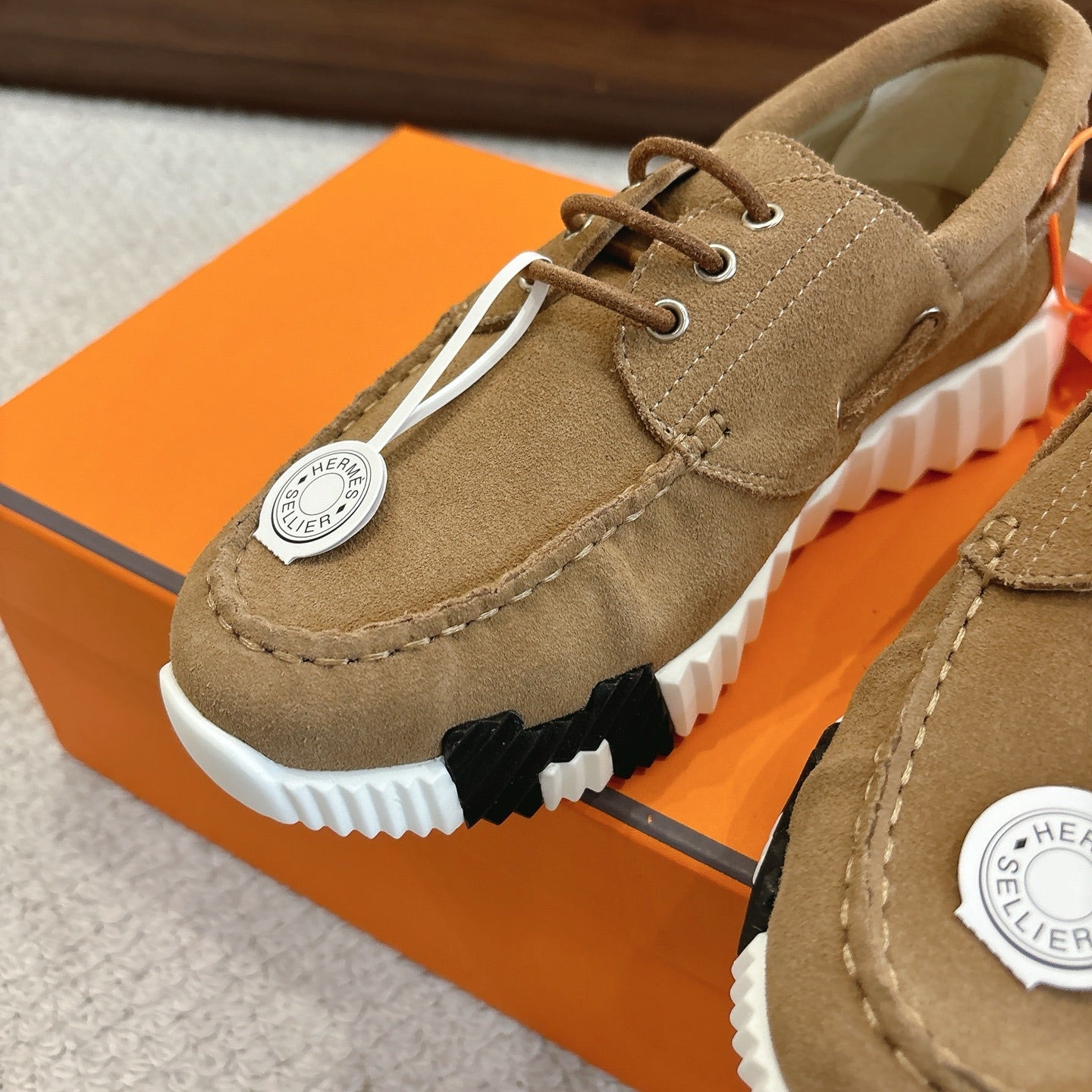 Tan suede lace-up sneaker close-up with white-and-black tread sole and round logo tag