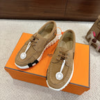 Tan suede lace-up sneakers with white ribbed sole and round logo charm on laces