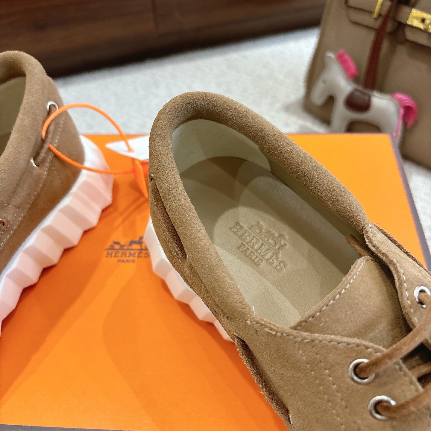 Tan suede sneaker with printed insole, lace-up front, and round logo charm