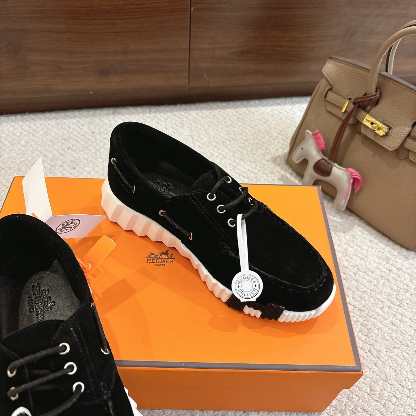 Black lace-up unisex shoe with white ridged sole and circular tag on lace