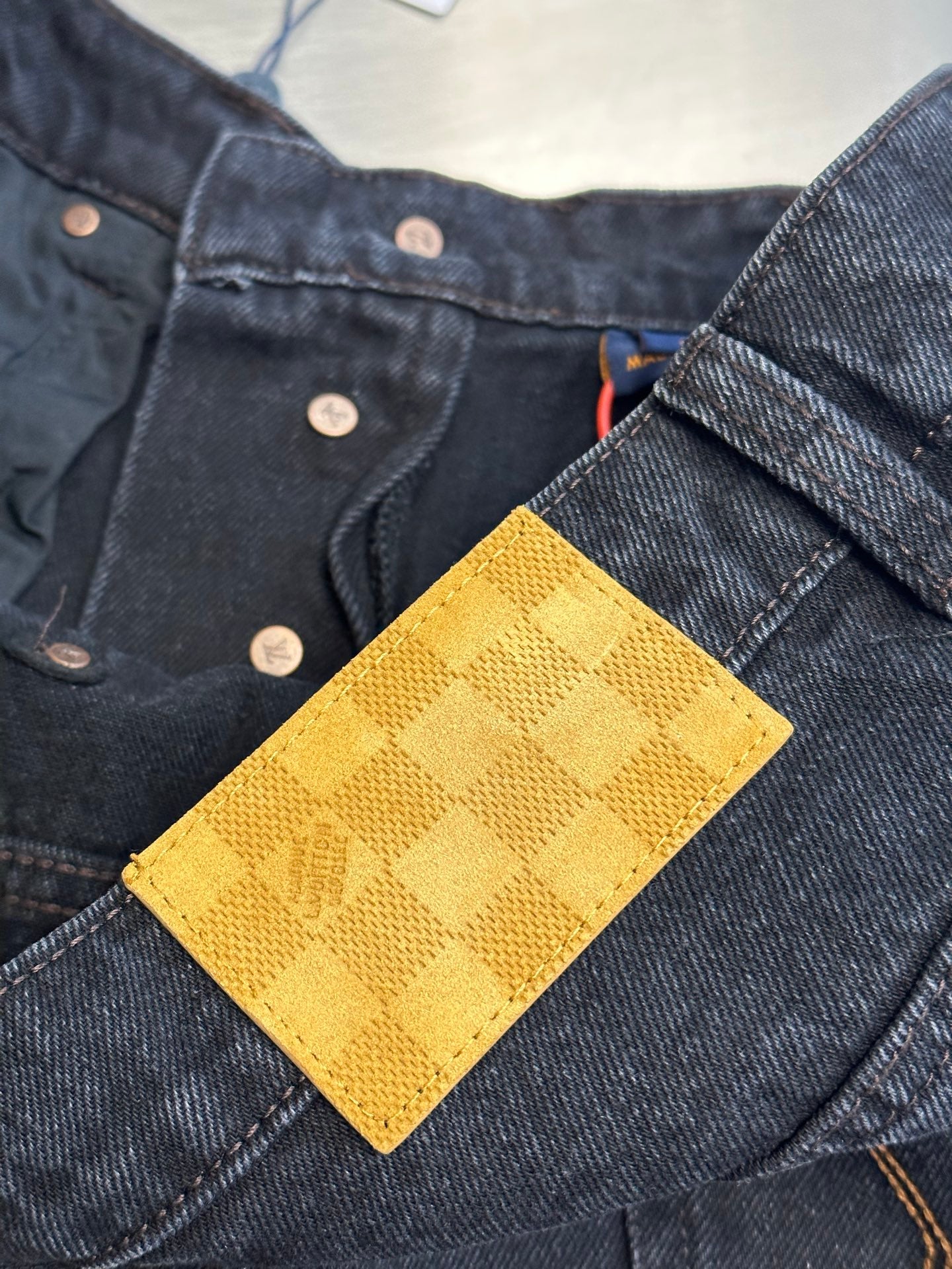 Dark blue denim pants with yellow check-pattern patch on the waistband