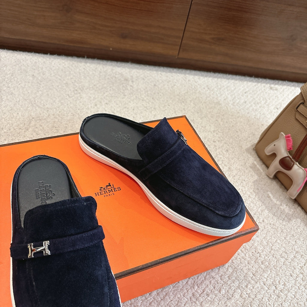 Hermes unisex suede loafers, dark blue with metal H buckle detail and white rubber sole.