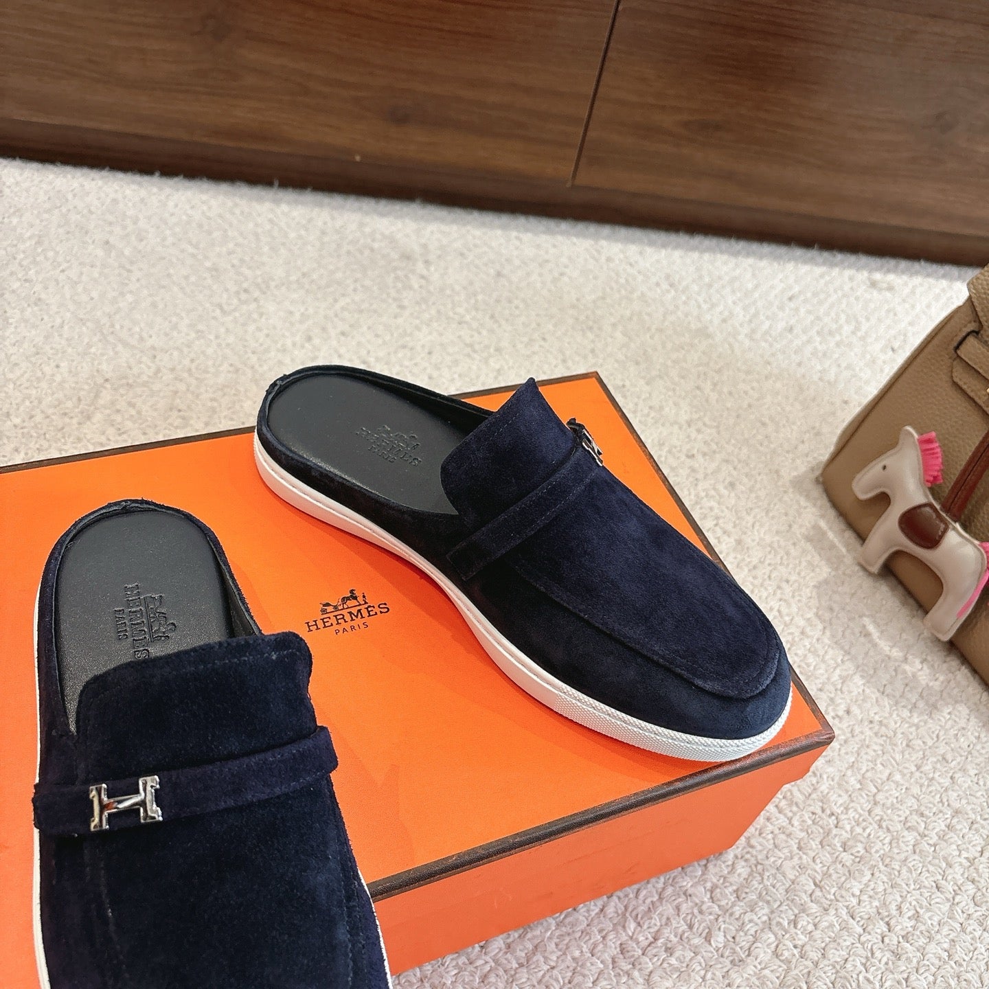 Hermes unisex suede loafers, dark blue with metal H buckle detail and white rubber sole.