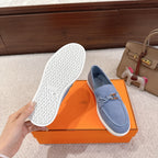 Blue suede loafers with white textured outsole and metal buckle strap, side view
