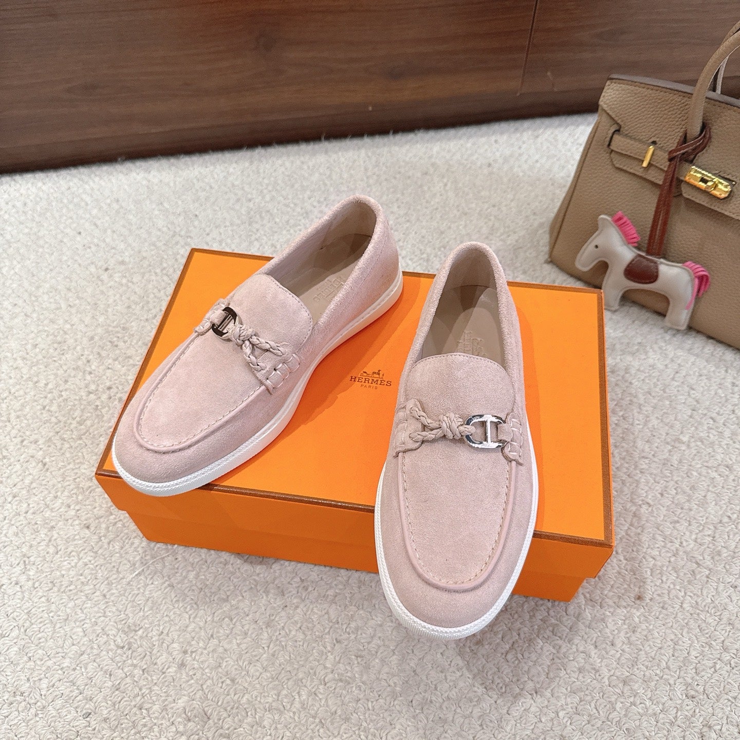 Hermes unisex light pink suede loafers, metal horsebit accent, white textured sole edge.