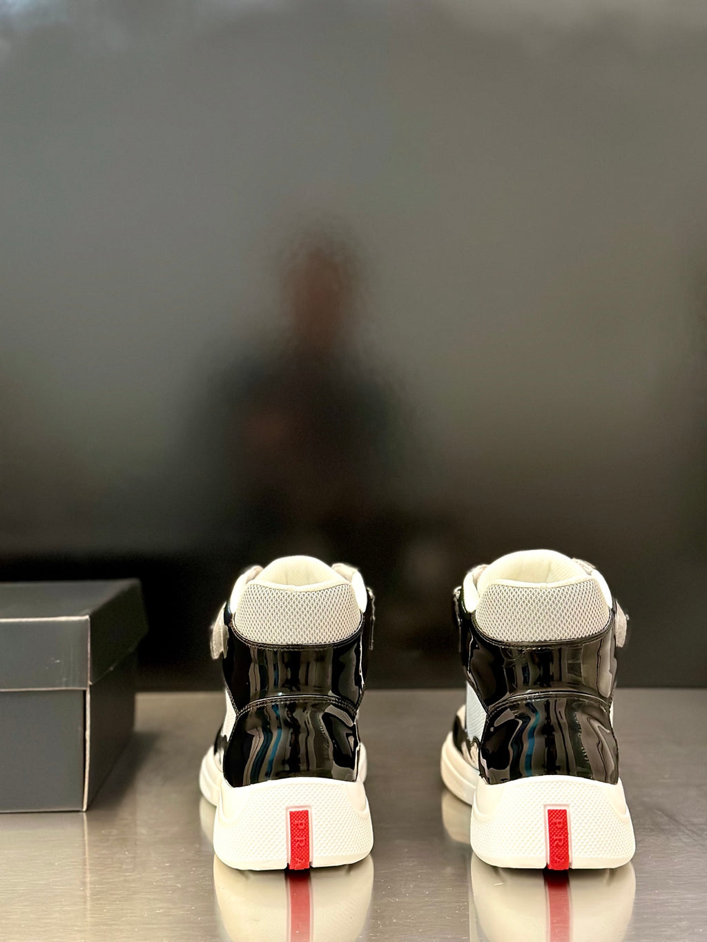 Prada unisex sneakers rear view, black glossy finish, white soles, red heel label