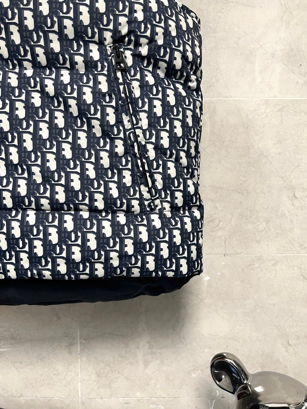 Logo-print puffer vest fabric with navy and white repeating monogram pattern