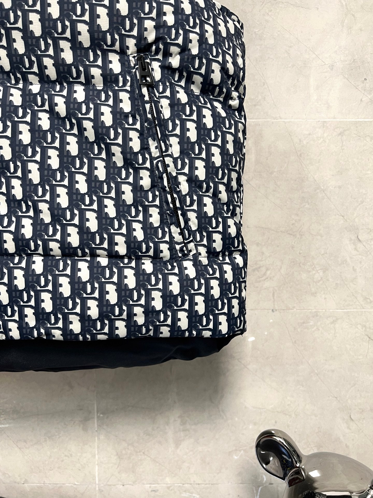 Logo-print puffer vest fabric with navy and white repeating monogram pattern