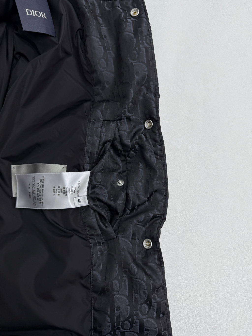 Dior long puffer jacket front close-up with Dior label, snap placket, dark monogram