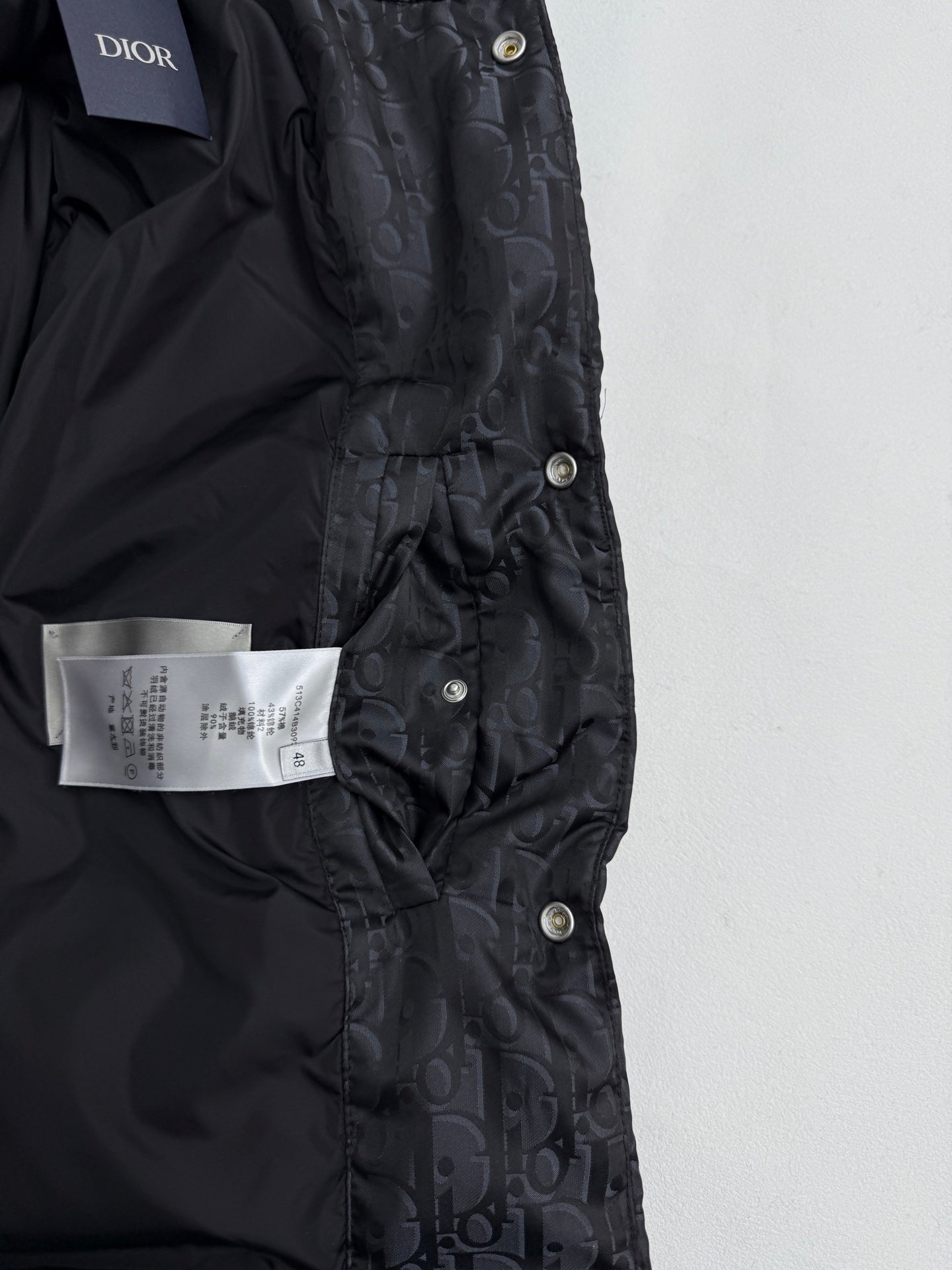 Dior long puffer jacket front close-up with Dior label, snap placket, dark monogram