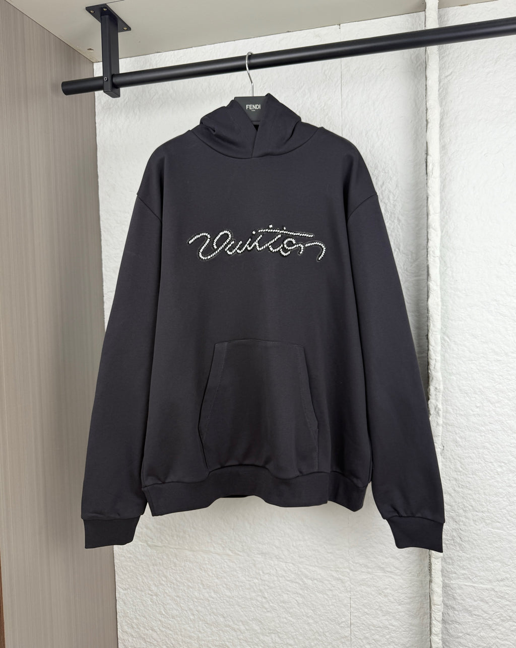 Black hoodie sweatshirt with hood, kangaroo pocket, and beaded "Vuitton" logo on chest