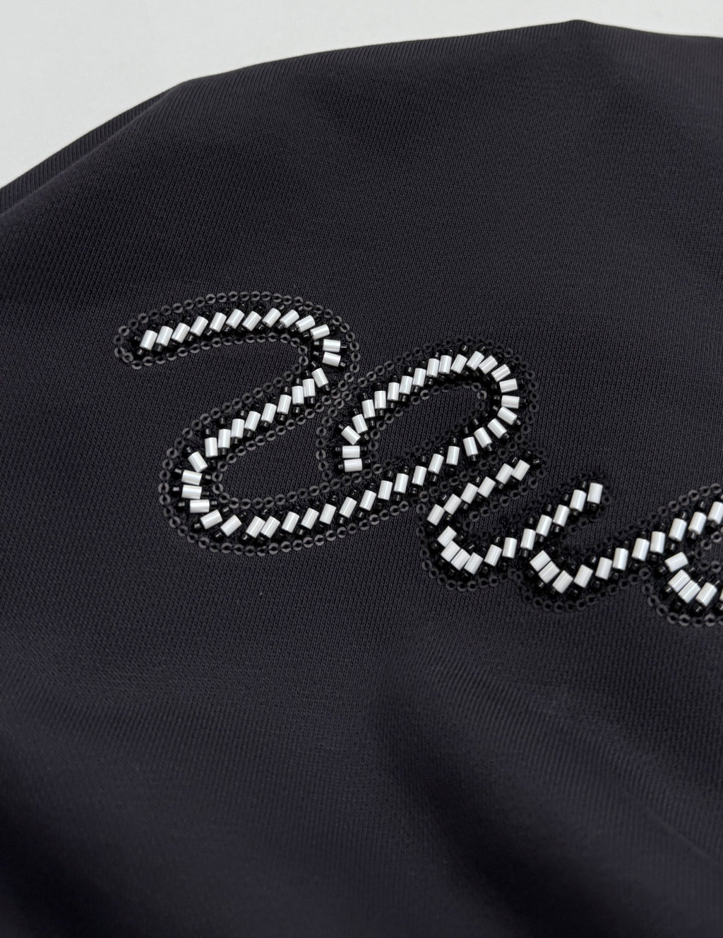 Black hoodie chest panel with large beaded "Vuitton" letter logo