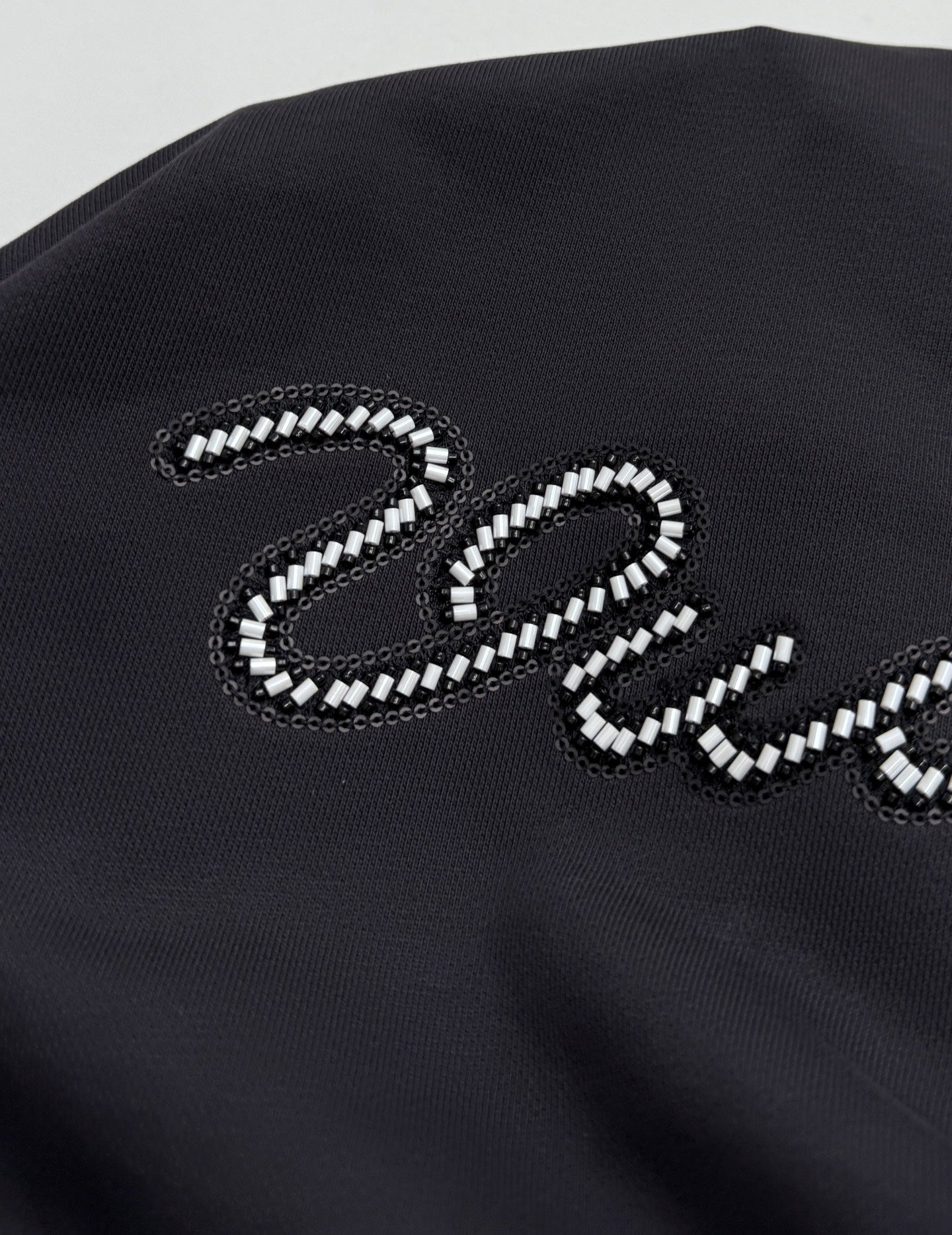 Black hoodie chest panel with large beaded "Vuitton" letter logo