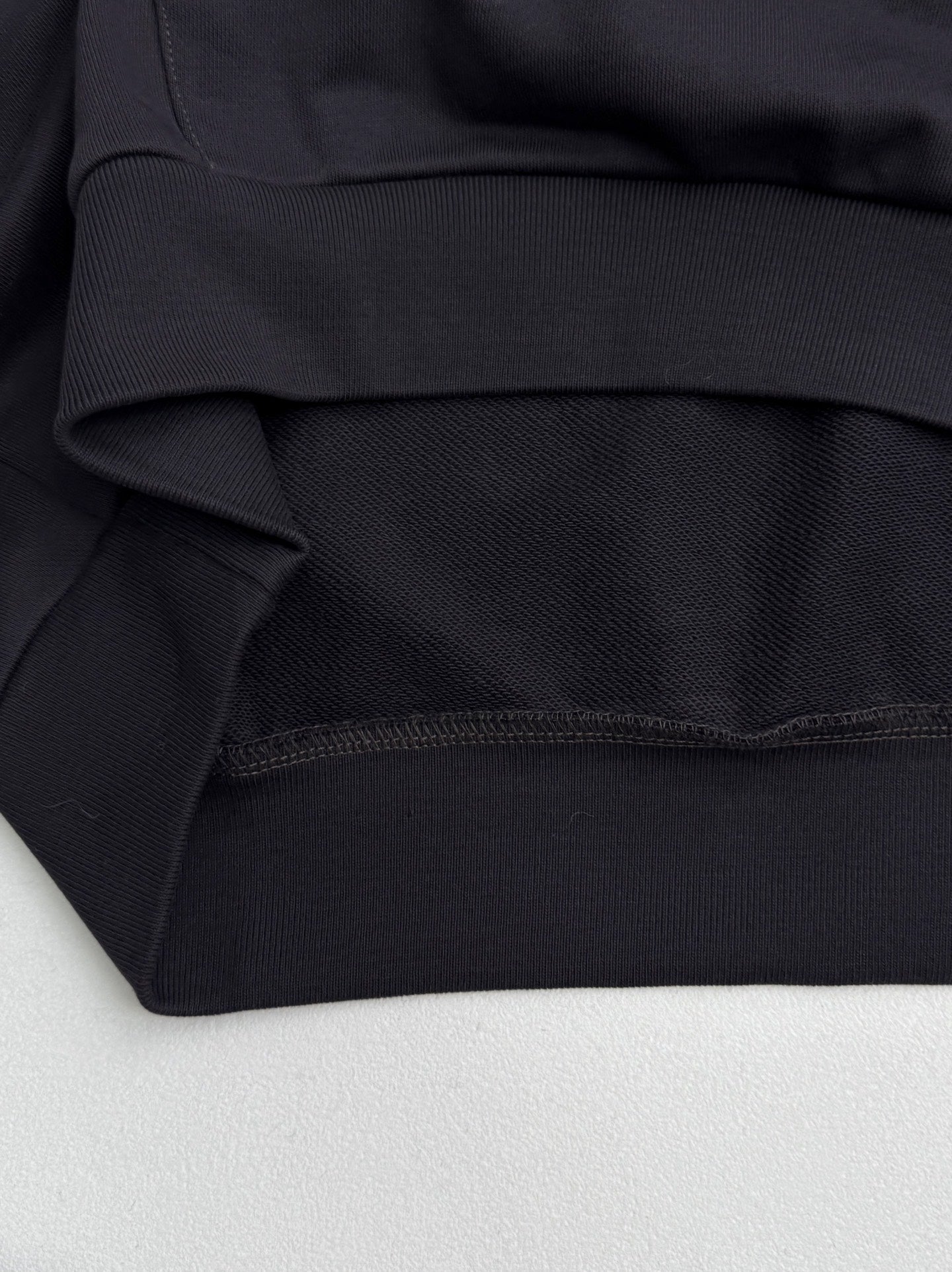 Black hoodie fabric close-up with ribbed waistband and stitched hem