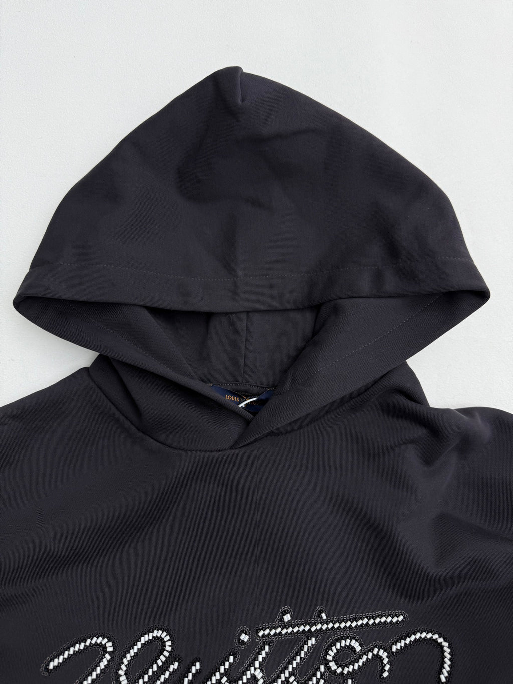 Black hoodie hood close-up with beaded "Vuitton" logo detail across the chest