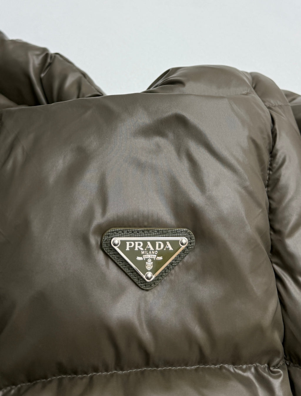 Prada triangle logo patch on olive puffer jacket with quilted stitching