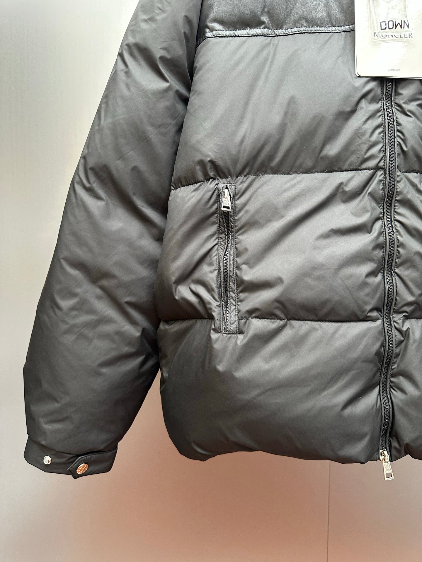 Moncler long puffer jacket side view with front pocket zippers and snap tabs