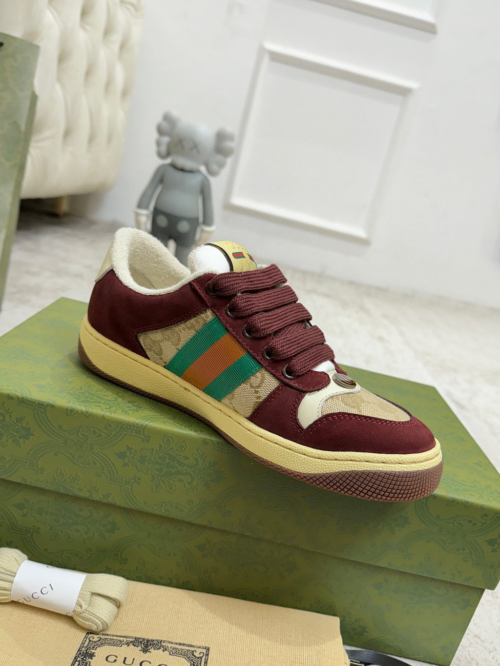 Pair of burgundy Gucci low-top sneakers on green box, lace-up with striped panel