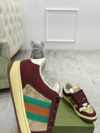 Burgundy Gucci low-top sneaker close-up of side patch, laces, and striped accent