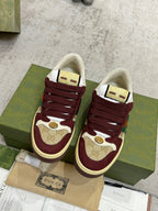 Burgundy Gucci low-top sneakers with striped insole detail, shown on shoe boxes