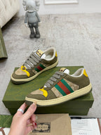 Gucci unisex sneakers held beside green box; olive leather with yellow and stripe accents