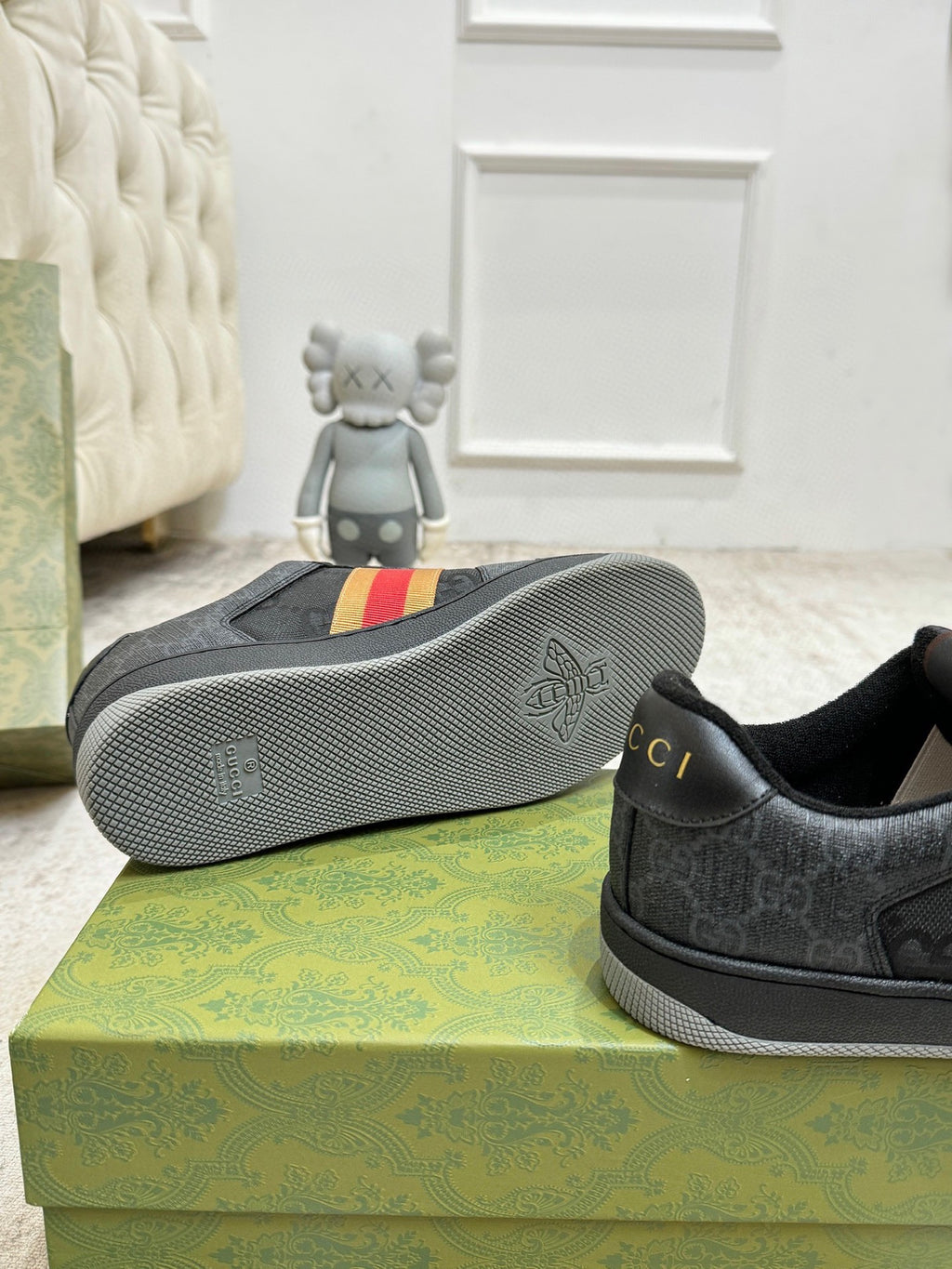 Gucci low-top sneaker outsole with tread texture and dark gray upper on display boxes