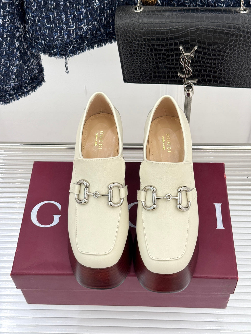 Cream Gucci loafers with metal horsebit detail, shown from front on a maroon box