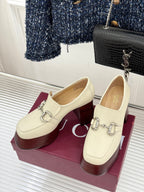 Pair of cream Gucci loafers on maroon boxes, featuring metal buckle horsebit detail