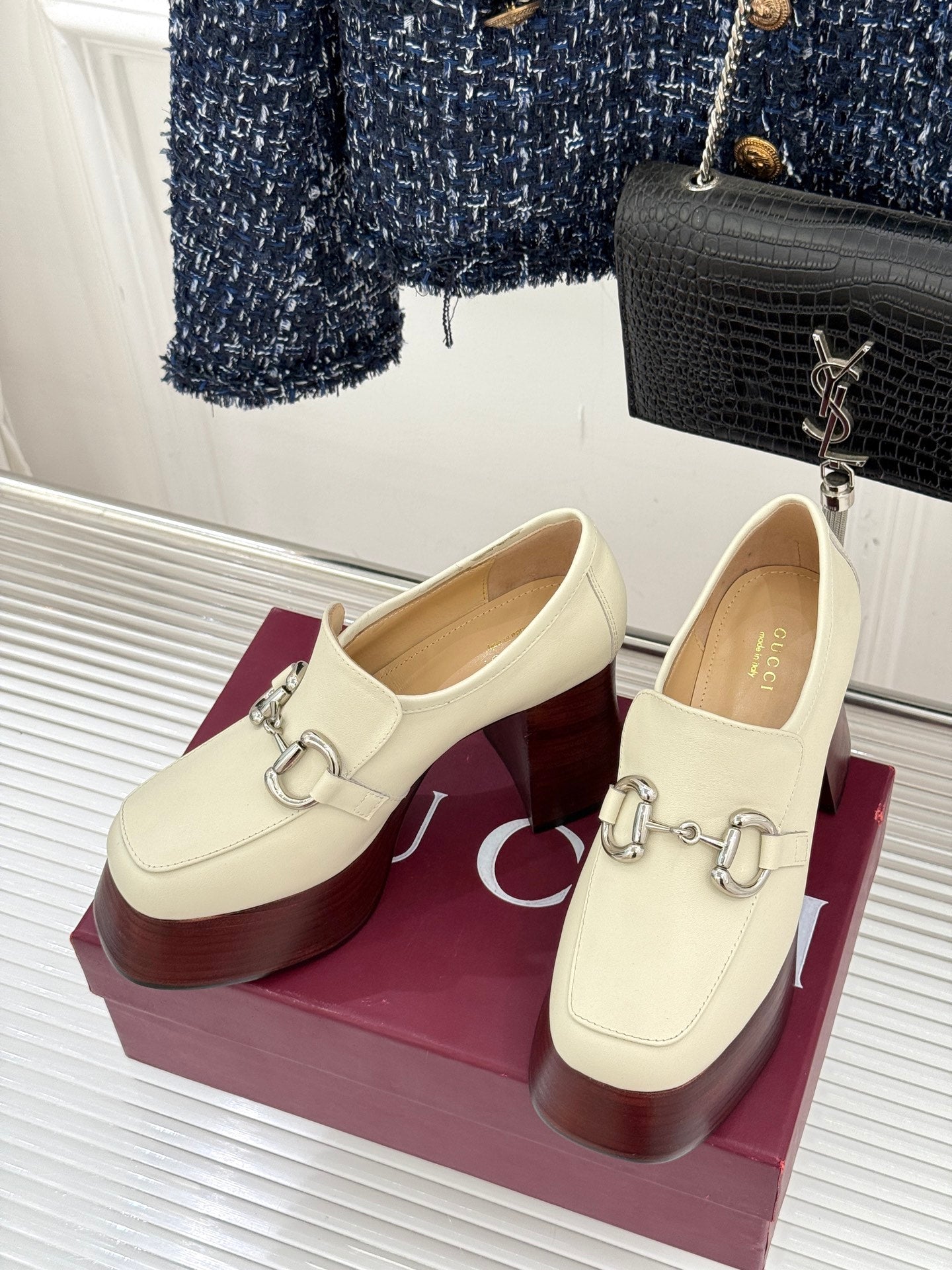 Pair of cream Gucci loafers on maroon boxes, featuring metal buckle horsebit detail