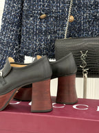 Close view of black leather loafers with tall block heels and silver chain detail