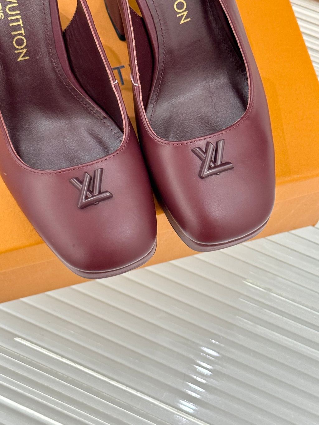 Close-up of burgundy leather high-heel pumps with monogram logo on toe