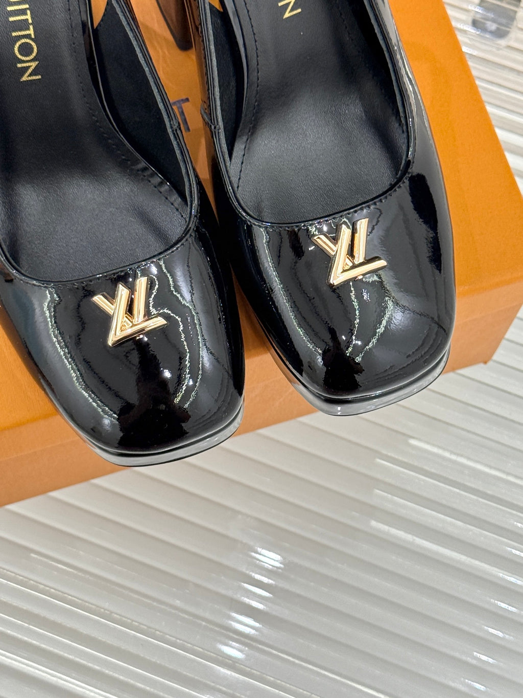Close-up of black patent leather pumps with LV logo on front