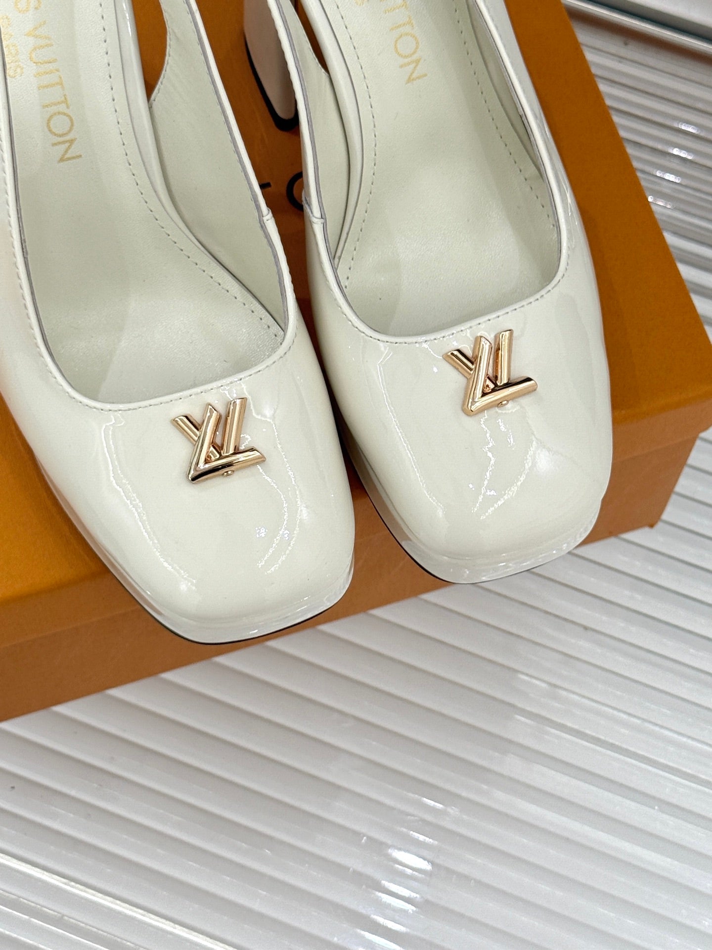 Close-up of white patent leather high-heel shoes with gold LV emblem