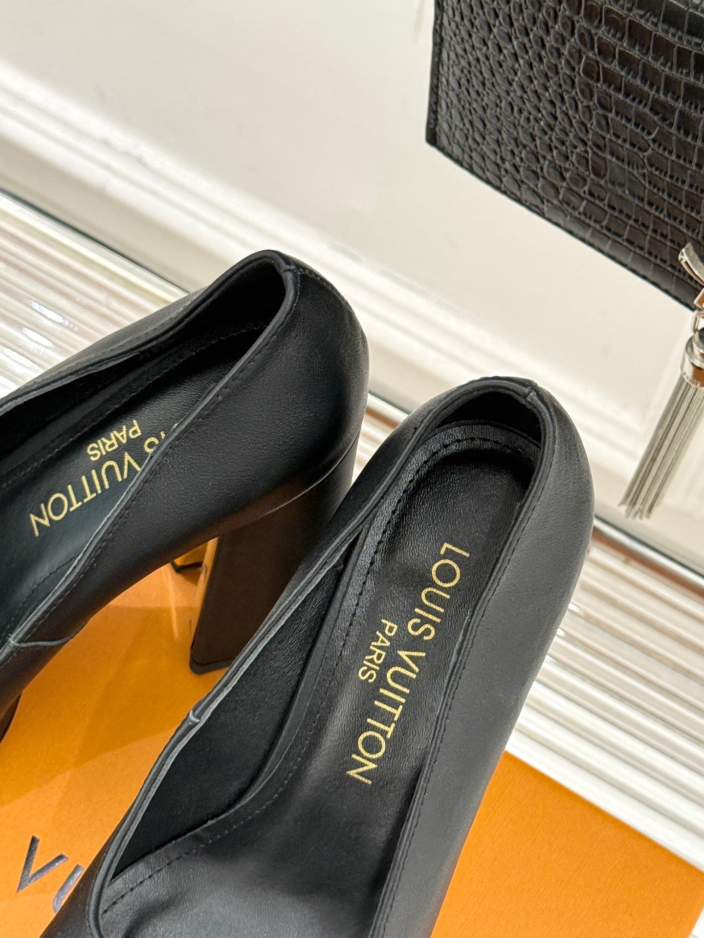 Black leather pumps showing side profile and gold-tone Louis Vuitton-style back branding
