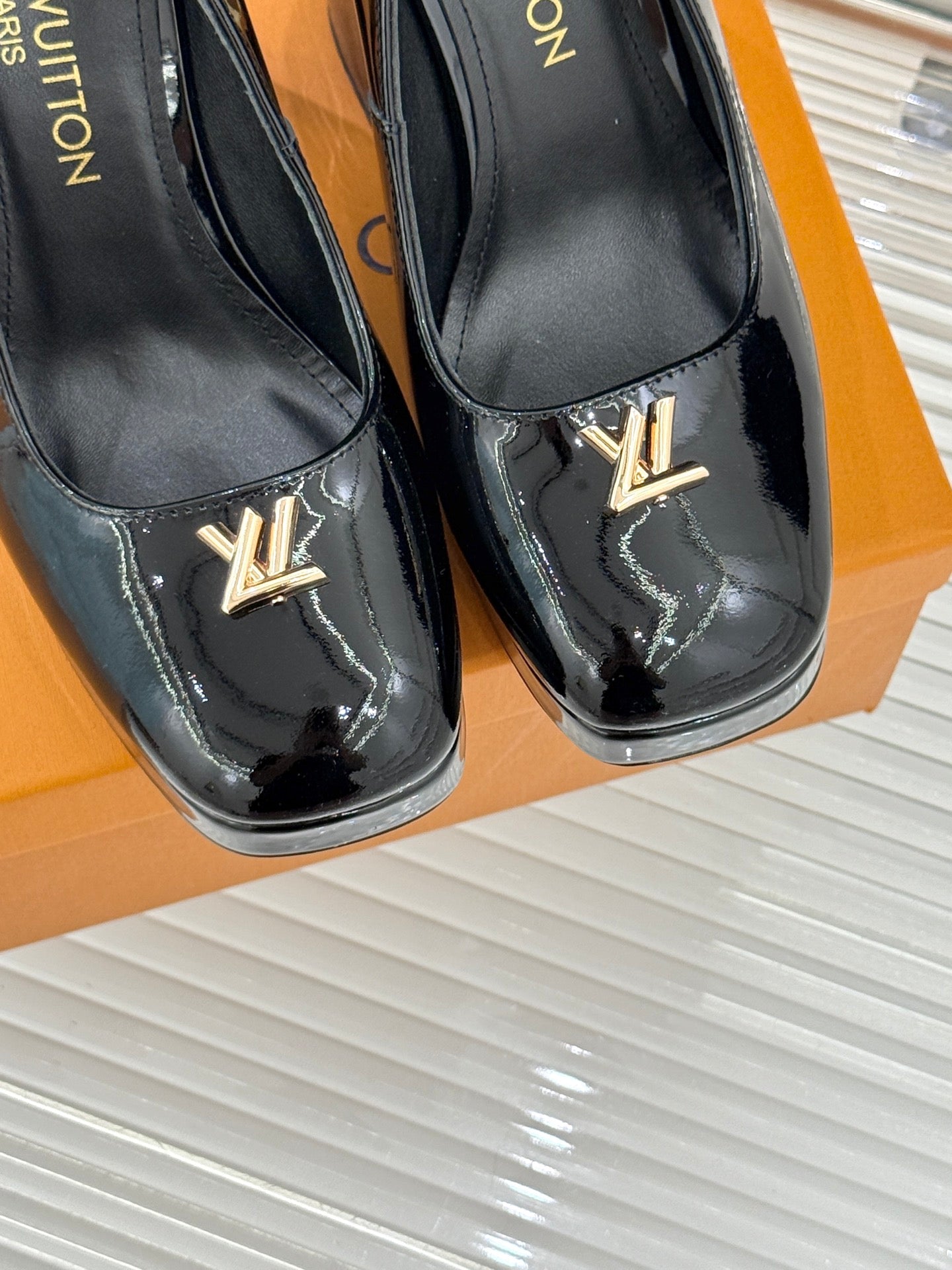 Louis Vuitton black patent pumps with gold LV emblems on the vamp, close-up pair
