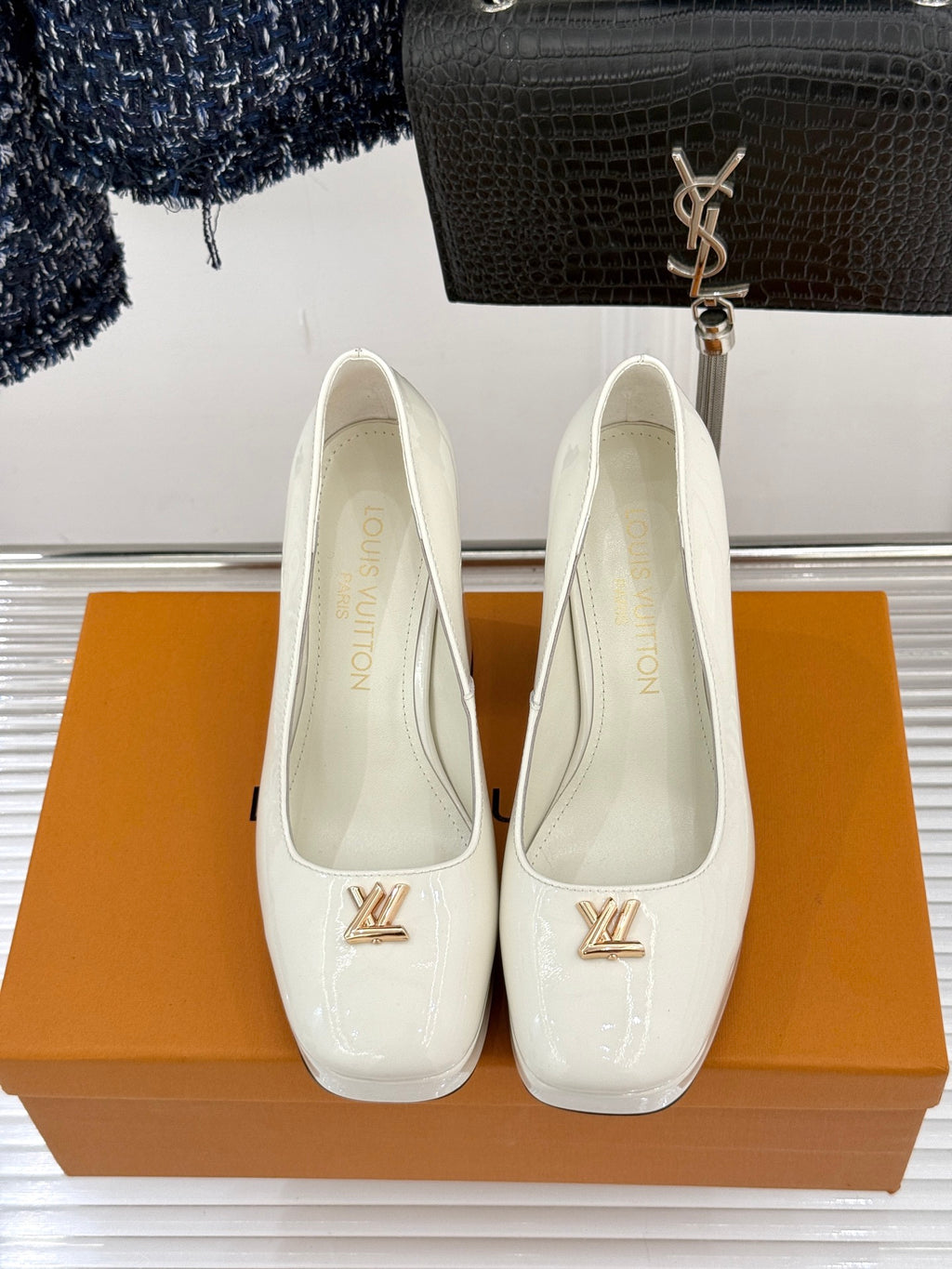 White leather pumps with rounded pointed toe, gold logo plaque, and mid-height heels
