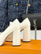 White leather heeled pumps with chunky block heels and gold logo detail at the toe