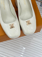 Close-up of white leather pumps with pointed toe and gold logo ornament on vamp