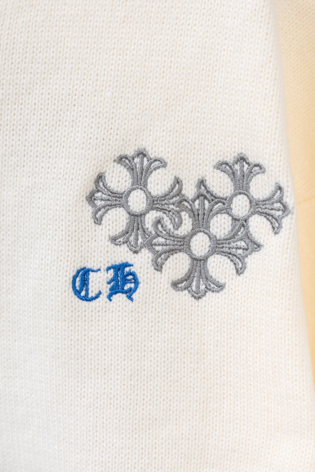 Close-up of gray flower embroidery and blue accent on a cream knit sweater